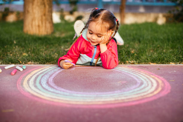 istock Girl drawing a rainbow with chalk on the sidewalk 1320219050