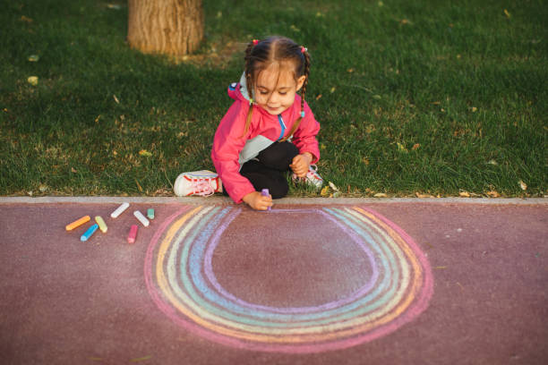istock Girl drawing a rainbow with chalk on the sidewalk 1320219176