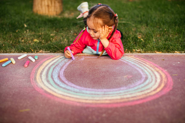 istock Girl drawing a rainbow with chalk on the sidewalk 1320219228