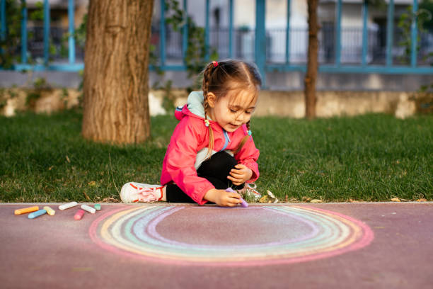 istock Girl drawing a rainbow with chalk on the sidewalk 1320219242