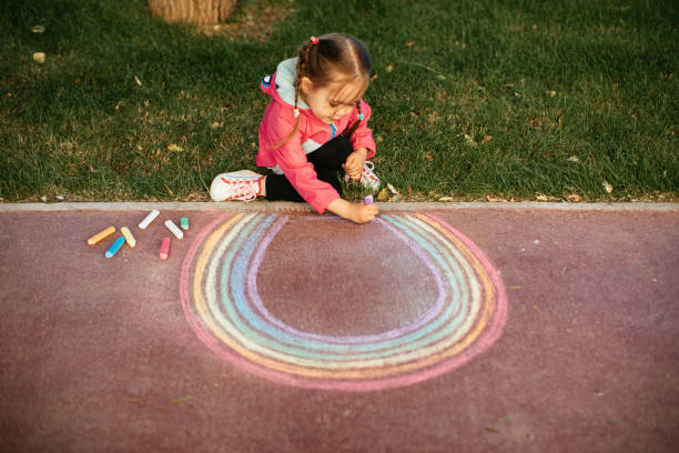 istock Girl drawing a rainbow with chalk on the sidewalk 1320219353