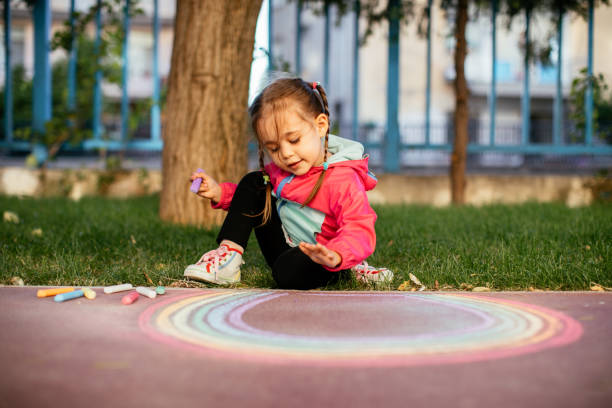 istock Girl drawing a rainbow with chalk on the sidewalk 1320219380