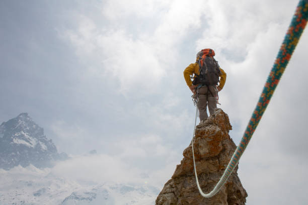istock Mountaineer on a rock pinnacle summit with rope, looking off 1320222561