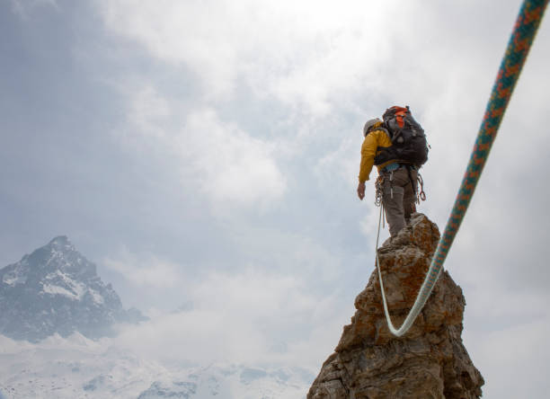 istock Mountaineer on a rock pinnacle summit with rope, looking off 1320223447
