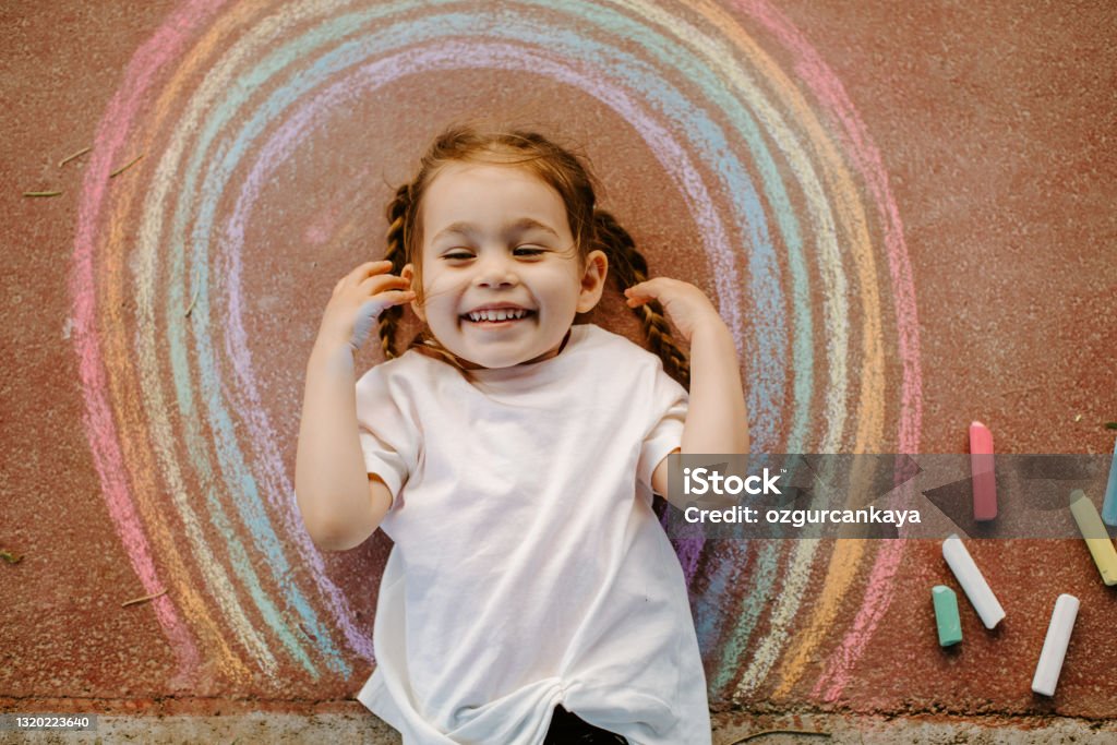 Child drawing rainbow with chalk Happy little toddler girl in rainbow painted with colorful chalks on ground or asphalt in summer. Cute child having fun. creative leisure Child Stock Photo