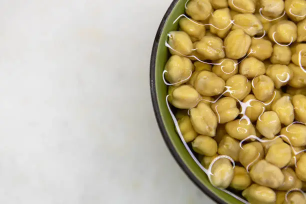 Chickpeas soaked in water, in bowl, on marble table. Concept of healthy eating, veganism, vegetarianism, meat and egg replacement. Prepare chickpeas before making hummus and other legume dishes.