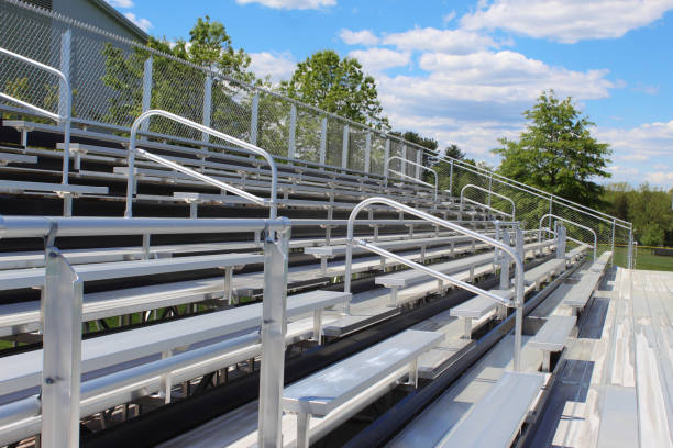 Empty metal bleachers during a sunny spring day with green trees and a blue sky in the background Metal bleachers during a sunny day; Relaxing on a nice day, watching a sports game; school bleachers stock pictures, royalty-free photos & images