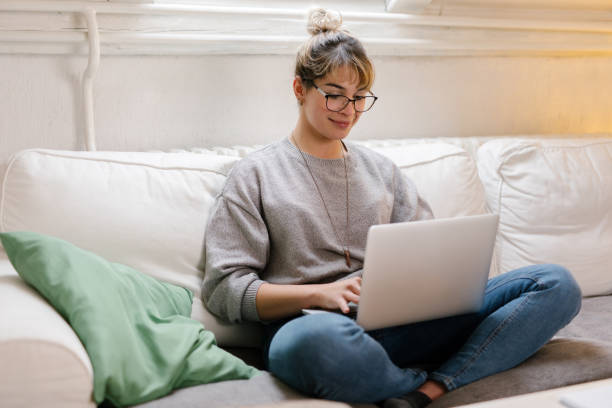 istock Young female student sitting and using laptop at home 1320227292