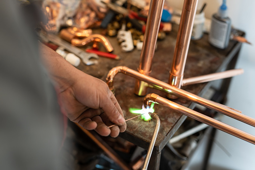 Close up on hands of unknown industrial worker plumber with central heating copper pipes welding using gas torch or blowtorch at work