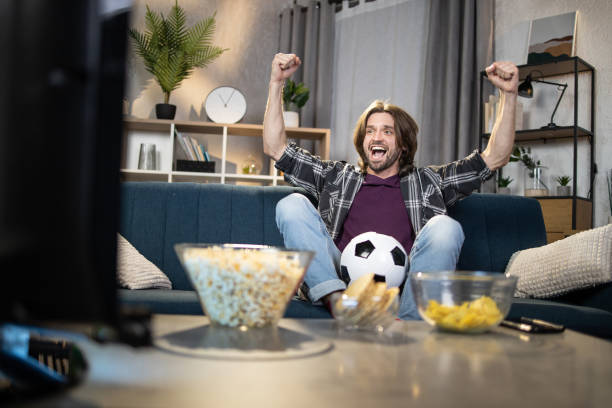 istock Man cheering favorite team while watching soccer on TV 1320229504