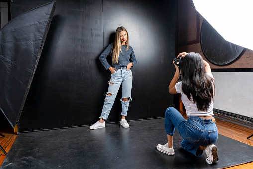 Horizontal portrait of a photo session of a model and a woman photographer in a photography studio, black background.