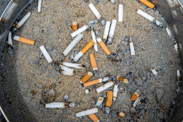 cigarettes are then left in the ashtray in smoking zone area. - brunt imagens e fotografias de stock