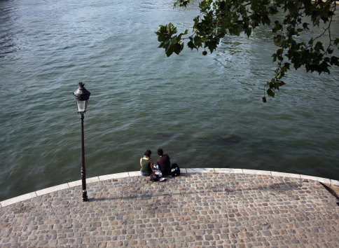 A boy and a girl sitting on the cobbled Seine bank on a sunny afternoon. Young couple having a relaxing break. 2009