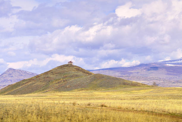 A gazebo on a hilltop in the middle of a plain against the backdrop of mountains under white clouds. Pure Nature of Siberia, Russia