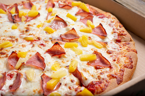 A view of a Hawaiian pizza inside a cardboard delivery box.
