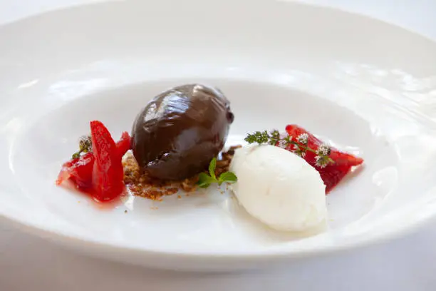 unusual dessert a ball of chocolate and a ball of cream with a couple of strawberry slices and some garnish