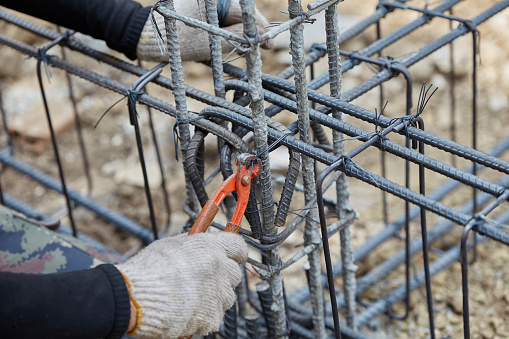 Cutting nips steel fixer pliers holding on construction worker hand while his hand wear a gloves. Skills worker using pliers to tied together rebar steel with wire rod. Close up and selective focus.