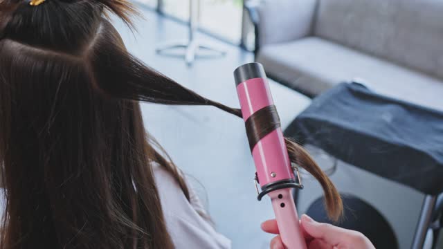 エキスパートマンスタイリストの手の使用カーリングアイロンのクローズアップ美容院で若い女の子の髪に巻き毛を作ります鏡を見ている認識されていない女性の顧客は理髪店で美容師.jpg (640×360)