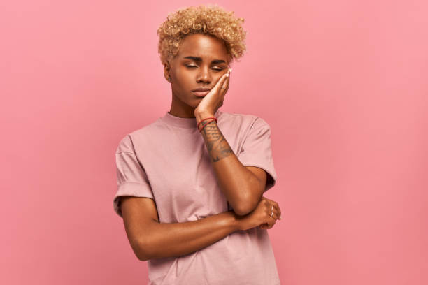 photo of tired dark-skinned female with blonde curly hair covers the face, closes eyes, feels fatigued, needs good rest, has sleepy expression, isolated over pink background. weariness and people - one person people boredom isolated imagens e fotografias de stock