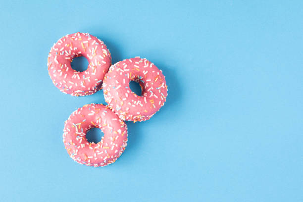 istock pink frosted donut with colorful sprinkles on blue background. copy space 1320265045