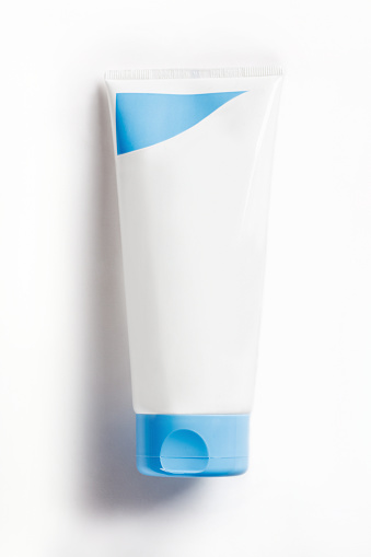 White hand cream tube with blue lid standing upside down on white background with shadow