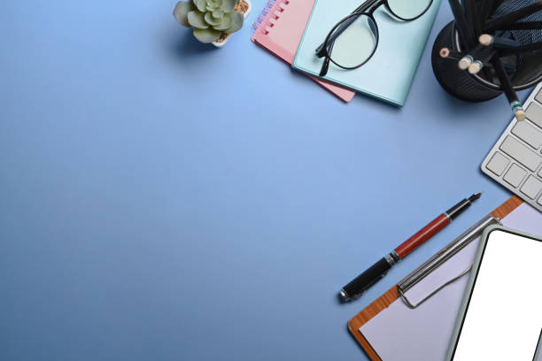 istock Above view of simple workspace with keyboard, notebook and pen on blue background. 1320268731