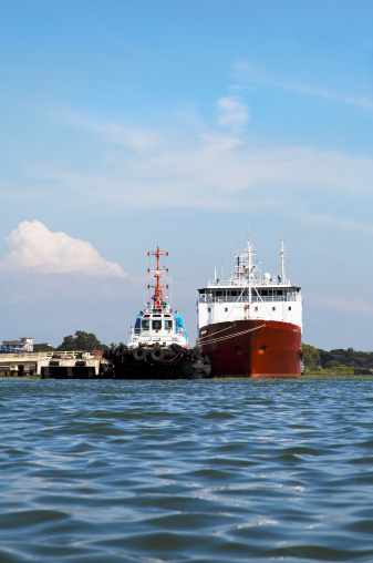 Ocean fareing ship moored at Kochi India with a tug, blue sky, clouds, portrait, copy space, vertical and crop margins
