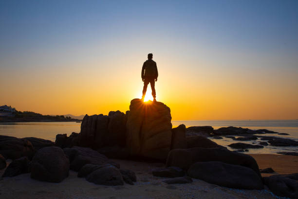 istock Young man standing on rock looking at sea sunrise 1320275616