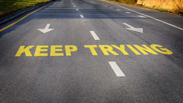 istock Keep trying word with white dividing lines and arrow on black asphalt road surface 1320281965