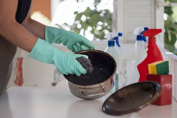 Woman trying to clean burnt pan with wire wool and lots of cleaners. Horizontal composition with copy space.