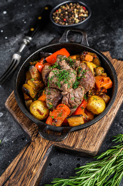istock Meat stew in cooking pot on dark rustic cutting board. Black background. Top view 1320284360