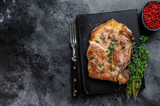 istock Grilled pork loin steak on a marble board. Black background. Top view. Copy space 1320284529
