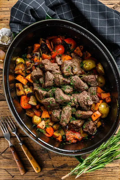Beef meat stew with potatoes, carrots and herbs. Wooden background. Top view.
