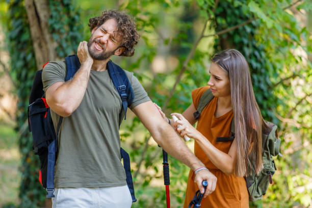 Man and his Wife are Scratching Itchy Skin due to the Attack of Insects in Nature. A Young Couple of Hikers with Backpacks have Problems with Itch Because of Large Group of Mosquitoes Attacking Them and They are Using a Preventive Spray. bug bite photos stock pictures, royalty-free photos & images