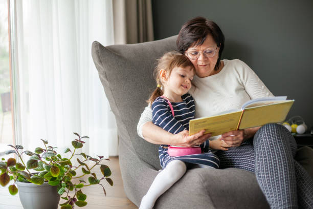 grandmother hugging her little granddaughter, reading a book - grandparent reading grandmother child imagens e fotografias de stock