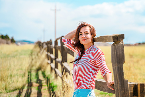 Beautiful woman leaning on a wooden fence, natural rustic landscape
