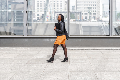 young black business woman with laptop walking in front of subway station Potsdamer Platz in Berlin