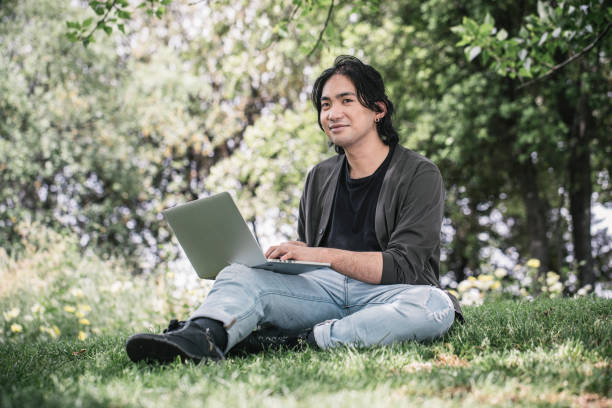 istock Young man works remotely using his laptop sitting on the grass at a park in springtime. 1320291403