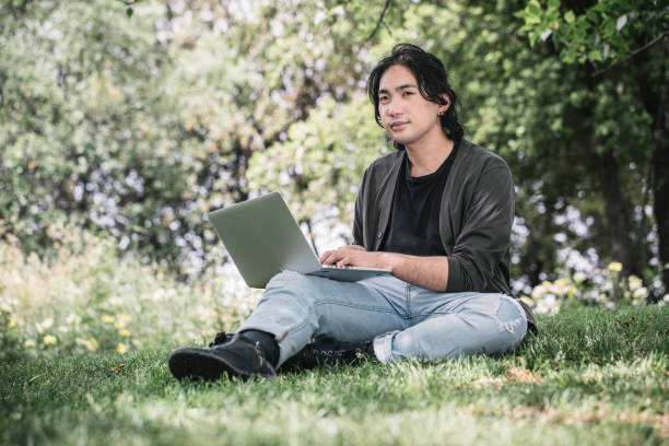 istock Young man works remotely using his laptop sitting on the grass at a park in springtime. 1320291481