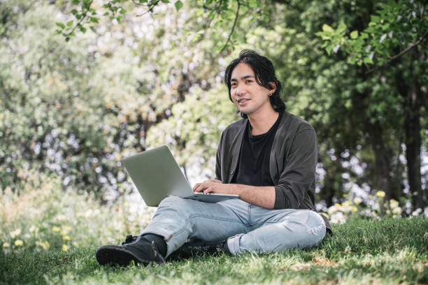 istock Young man works remotely using his laptop sitting on the grass at a park in springtime. 1320291484