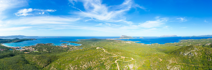 View from above, stunning aerial view of a mountain range covered by a green vegetation with Tavolara Island in the distance bathed by the mediterranean sea. Sardinia, Italy.