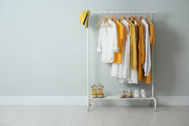 Rack with bright stylish clothes, hat and shoes near light grey wall indoors, space for text Rack with bright stylish clothes, hat and shoes near light grey wall indoors, space for text garment store fashion rack stock pictures, royalty-free photos & images