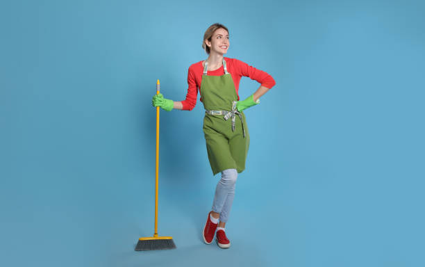 istock Young housewife with broom on light blue background 1320296777