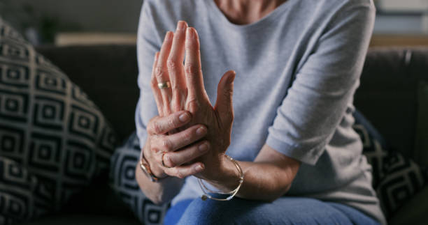 Cropped shot of an unrecognizable woman sitting alone at home and suffering from arthritis in her hands stock photo