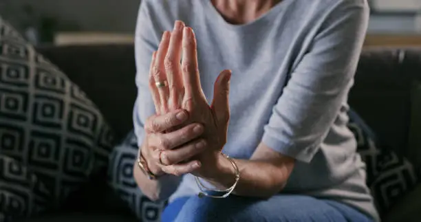 Photo of Cropped shot of an unrecognizable woman sitting alone at home and suffering from arthritis in her hands