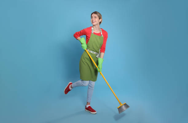 istock Young housewife with broom on light blue background 1320297235