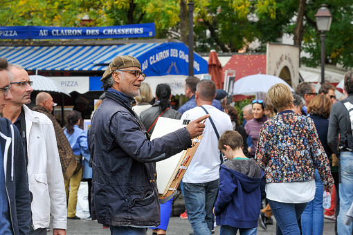 Paris, France, September 29, 2017: The Montmartre art market attracts tourists as well as locals. There are many types of art and everything that goes with a flea market. Visitors and dealers alike enjoy the hustle and bustle. A painter is looking for a model.