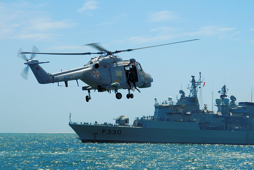 Setubal, Portugal: Portuguese Navy Super Lynx Mk.95 helicopter with diver on the door, approaching frigate F330, NRP Vasco da Gama, built by Westland Helicopters. Portuguese Naval Aviation. Two Lynx can be operated from the flight deck of a Vasco da Gama-class frigate.