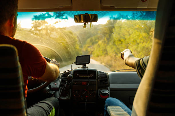 Rear view of unrecognizable boy pointing at beautiful scenic nature view during a ride in a campervan with his father driving.