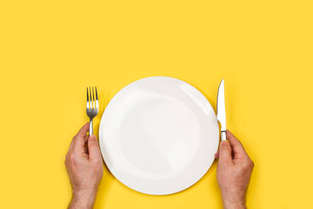 istock Man hands holding fork and knife on a white plate 1320307842